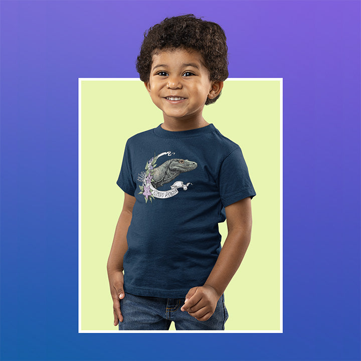 Toddler on blue and green background wearing tee shirt with a komodo dragon on it.