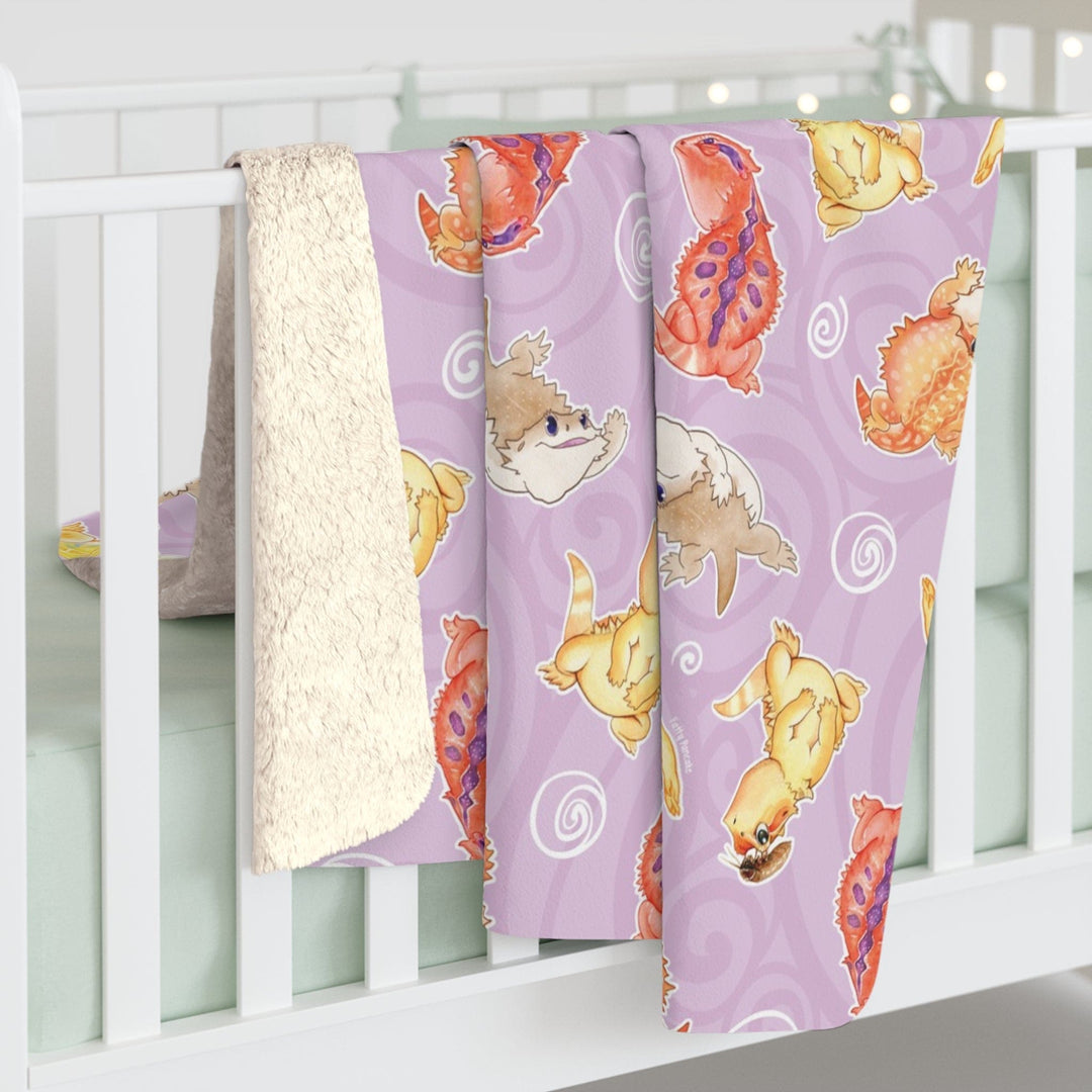 Bearded dragon sherpa blanket with 4 different bearded dragons doing silly things: leaping, giving stink eye, flattening their body, and one with a roach on it's head. The background of the blanket is soft purple with white lineart of swirls.