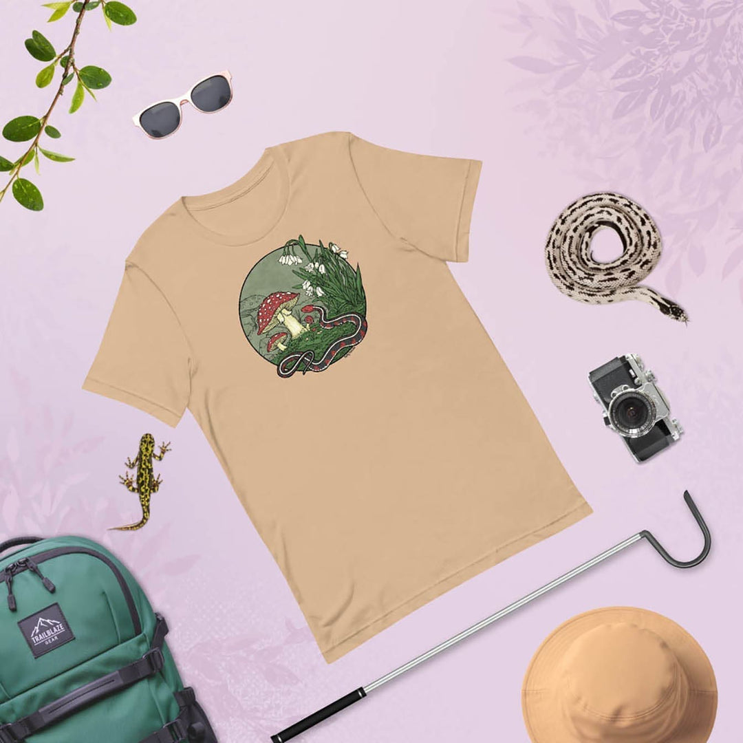 Beige t-shirt with nature-themed graphic of a snake. The tee is surrounded by outdoor items on a light purple background.