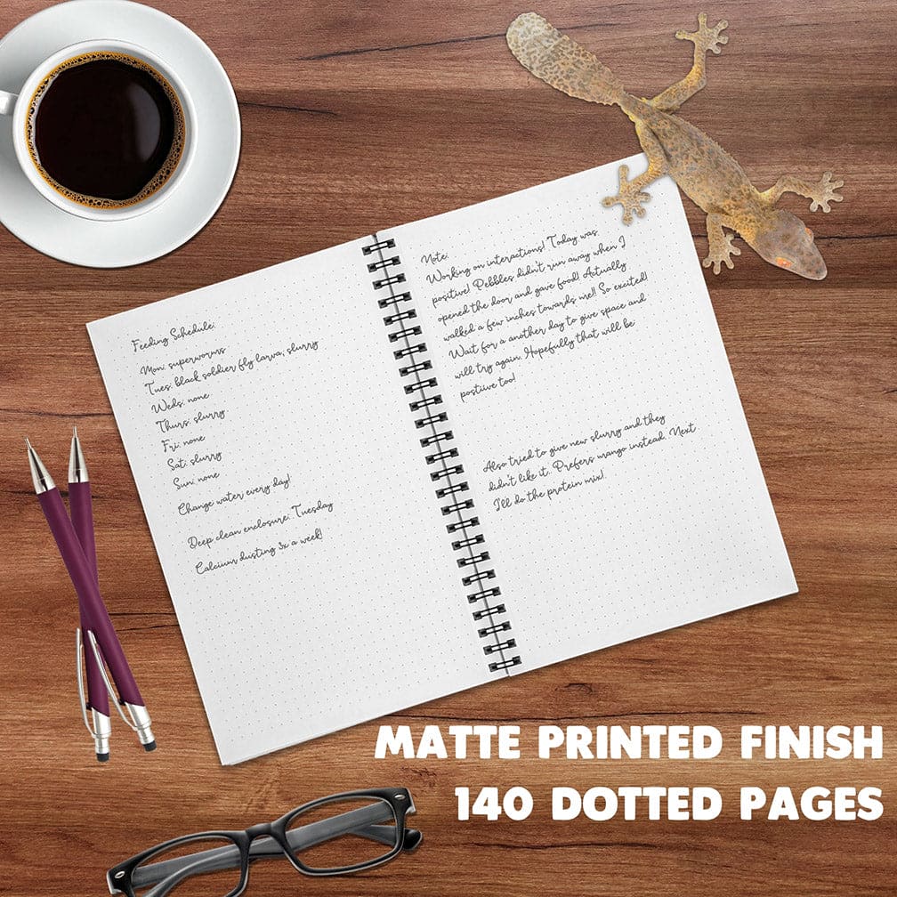 An open spiral-bound notebook with a matte white page finish lies on a wooden desk, surrounded by a cup of black coffee, two purple pens, eyeglasses, and a leaf tailed gecko. Large text at the bottom reads &
