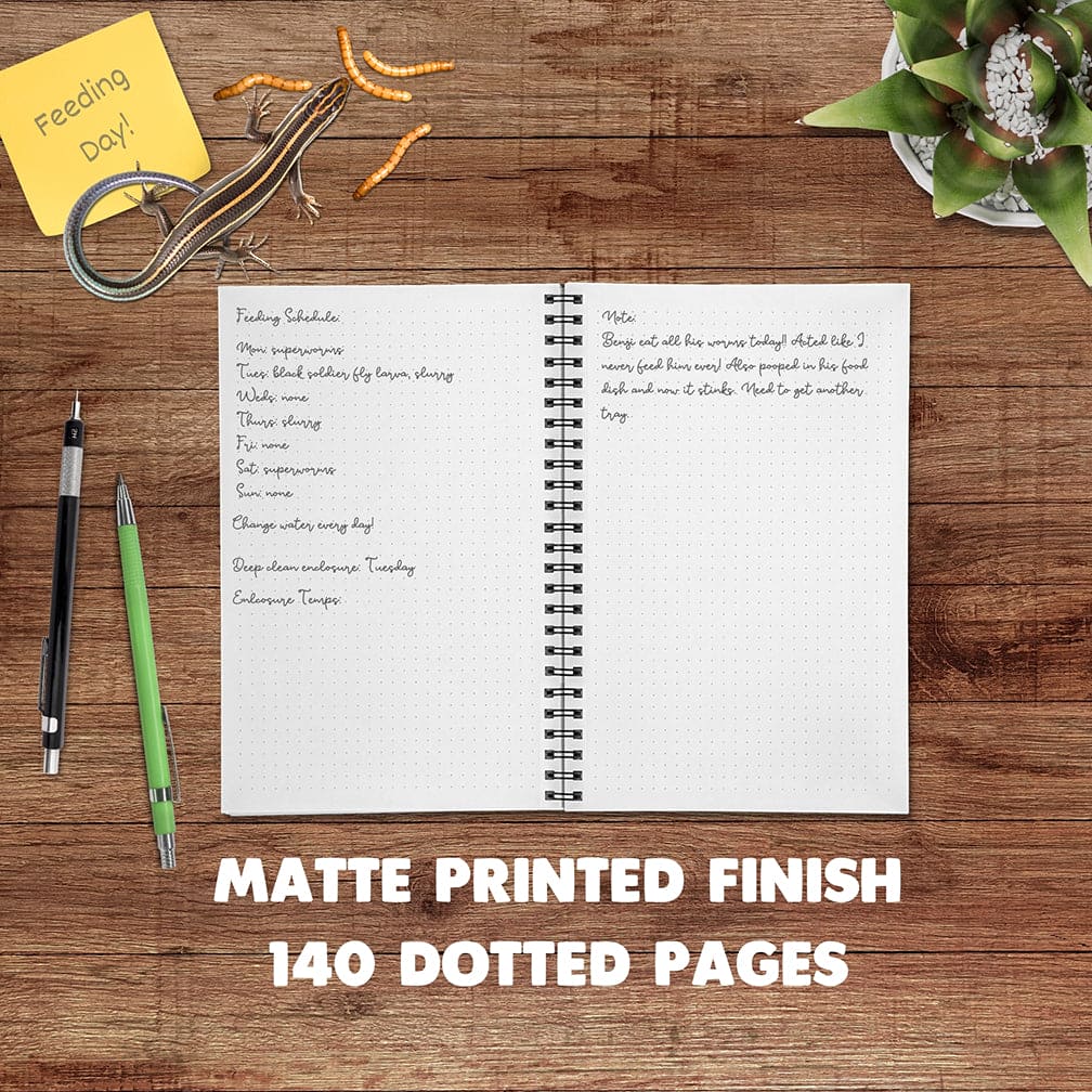 An open spiral-bound planner or notebook with a white matte paper cover spread on a wooden desk, surrounded by pens, a sticky note, a lizard eating worms, and a desk plant. Large text at the bottom reads &