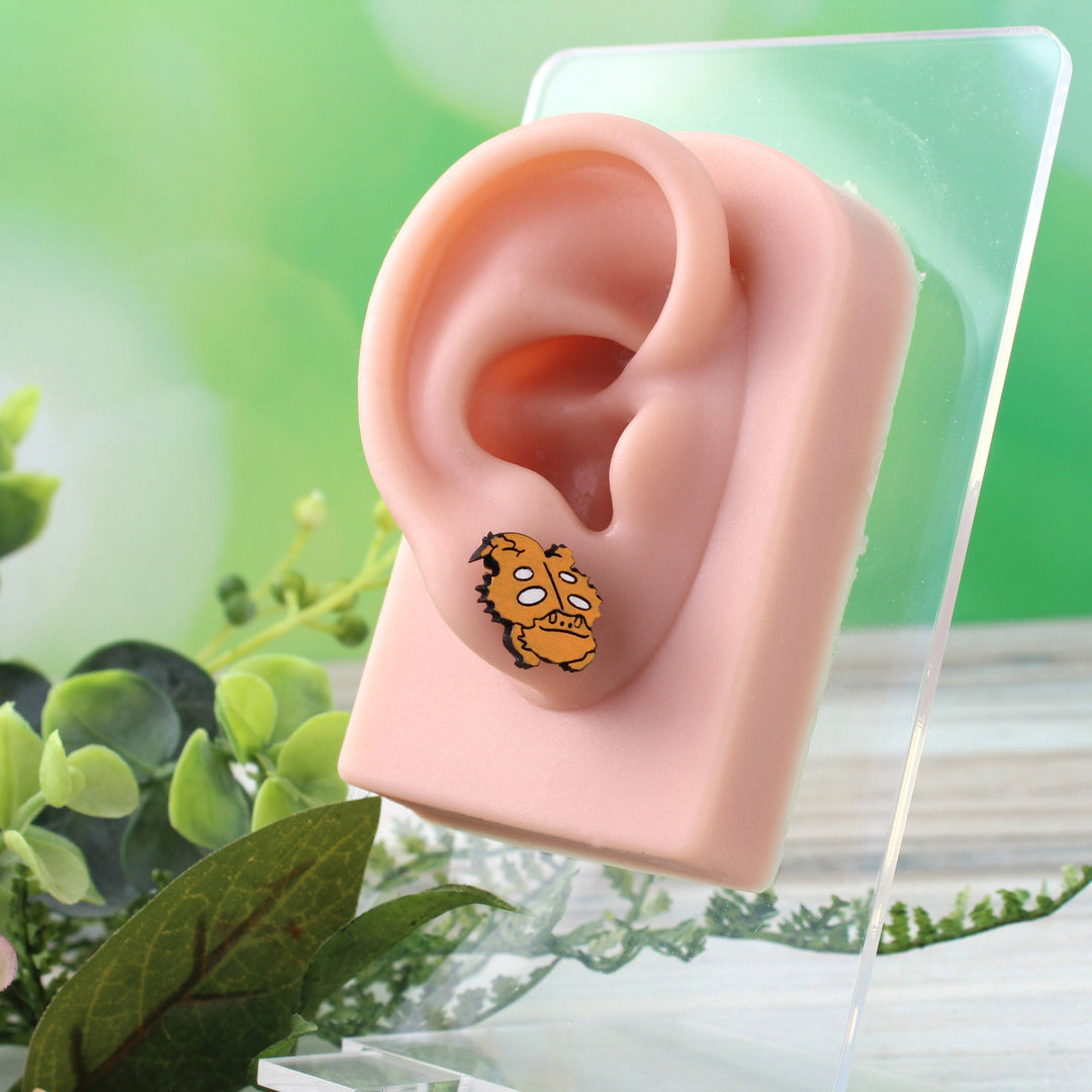 Orange and white cartoon bearded dragon stud earrings. The earrings are shown on a model ear.