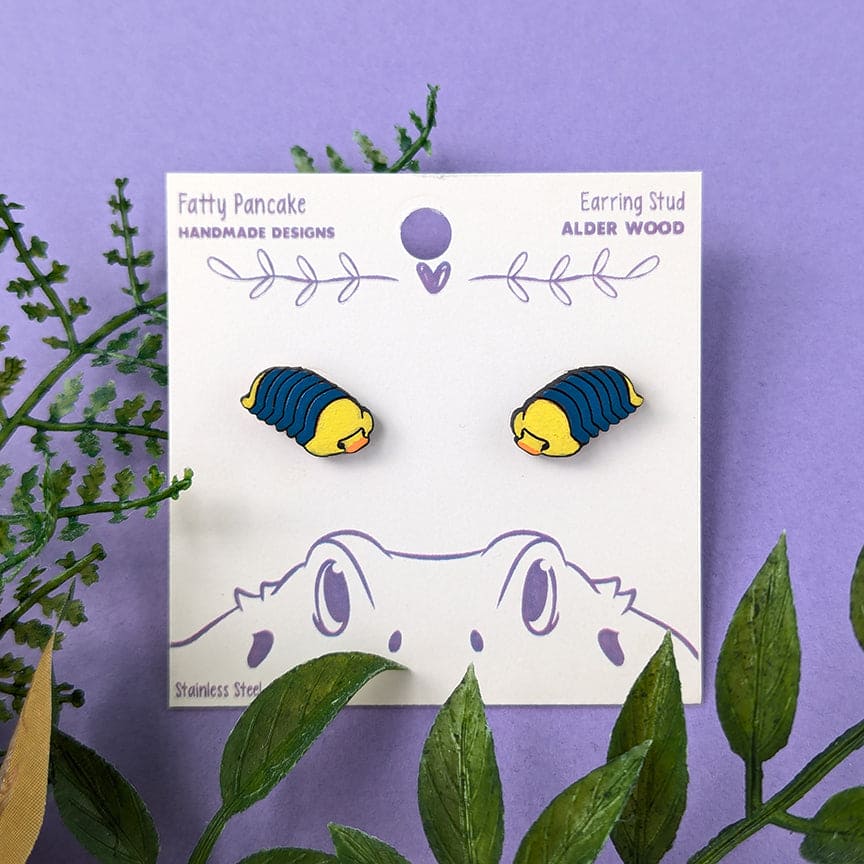 Rubber Ducky laser cut earring studs, cut with Alder wood and hand painted using acrylic paint pens. The background is purple with fake plants surrounding it.