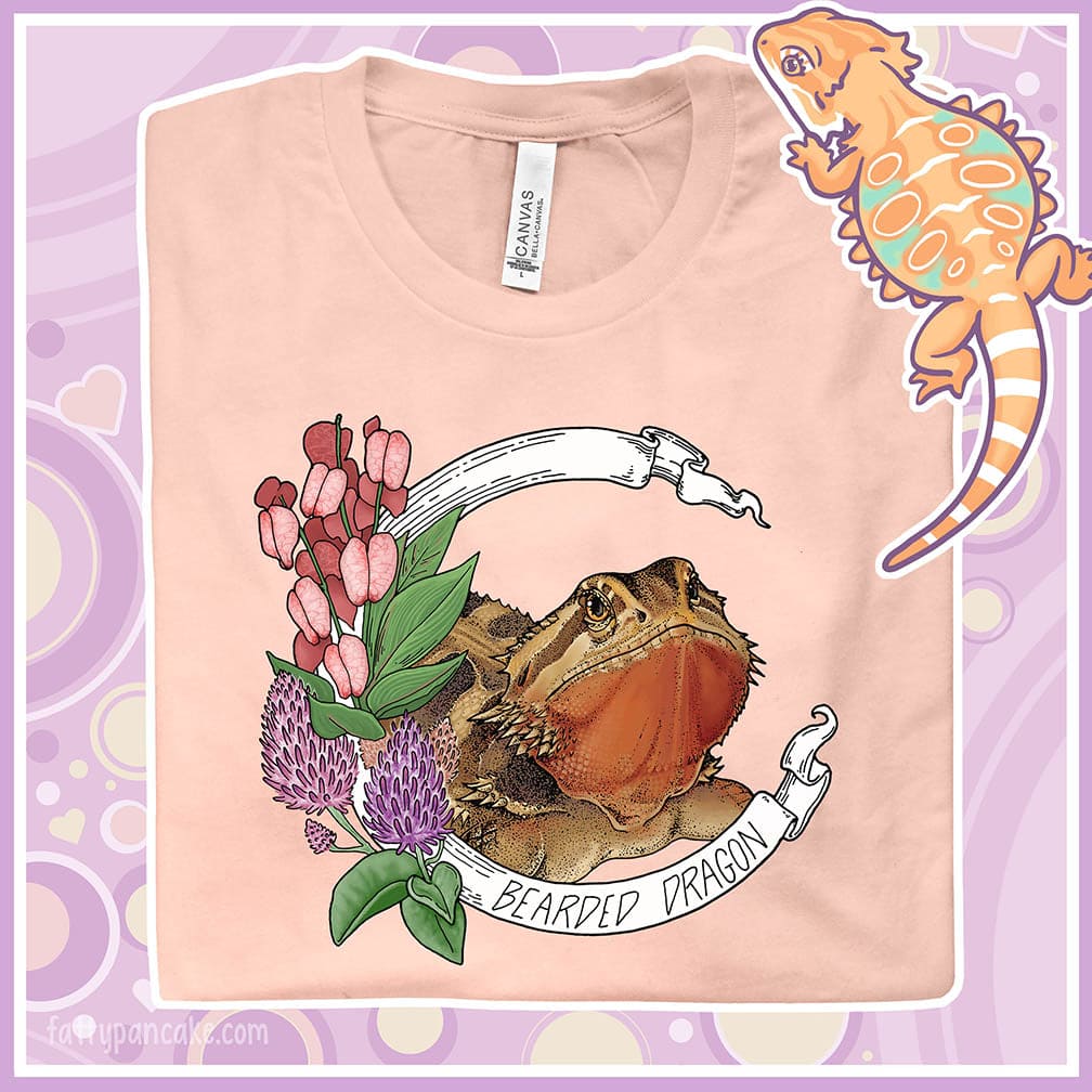 Close up of a folded crew neck tee with a bearded dragon on it. The beardie is framed by a white banner with the text, "Bearded dragon" on the bottom and purple and red flowers adorning the left side of the design.