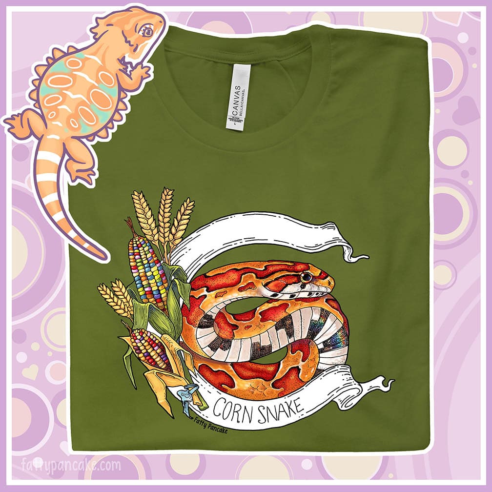Mockup of an olive colored crew neck tee showing a closeup of a corn snake graphic. The snake is vibrant red and orange with colorful glass corn with lots of different colors in it. A white banner frames the design with "Corn Snake" text on the bottom of the banner.