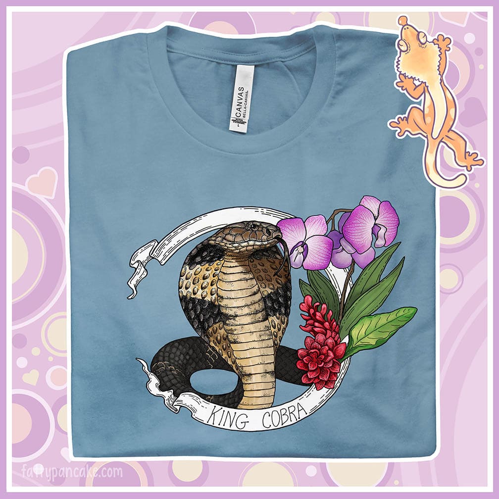 A folded cream colored crew neck tee with a king cobra hooded out and orchids and red flowers on the right side. A white banner reads King Cobra on the bottom.