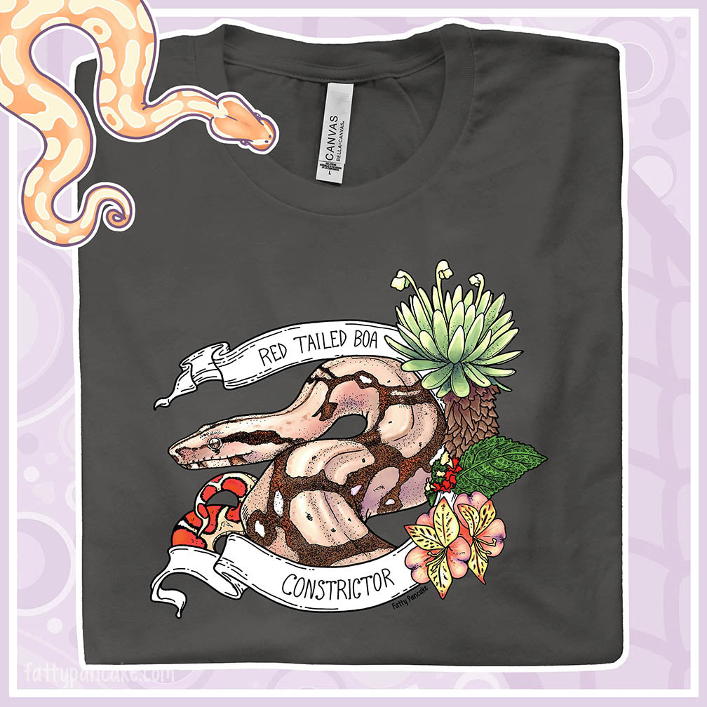Grey t-shirt with a red-tailed boa constrictor design framed by a white banner with a pink and yellow flower and a broad leafed plant, resting on a light purple background