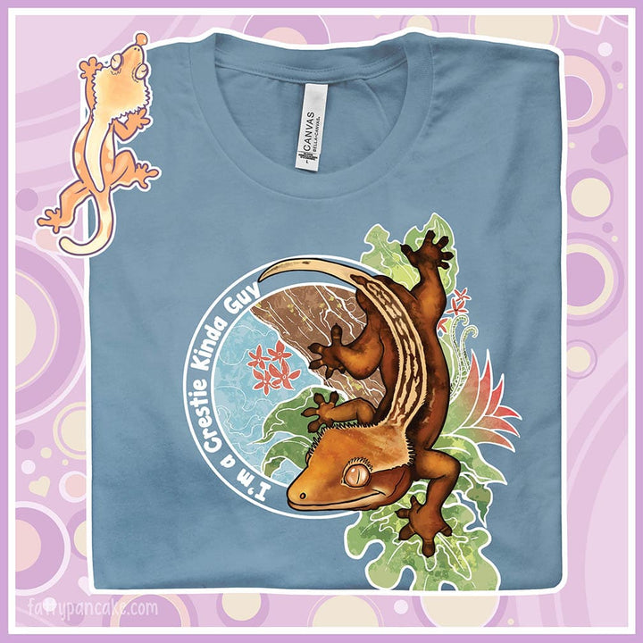 A folded crew neck tee showing an enlarged image of a graphic of a crested gecko climbing down from a tree with the words "I'm a crestie kind of guy" on the left hand side.