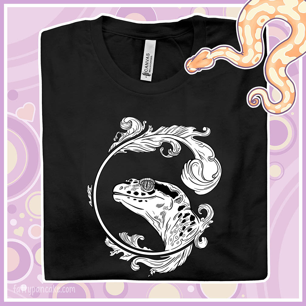 A folded black crew neck tee of a black and white leopard gecko surrounded by a beautiful flourish design.