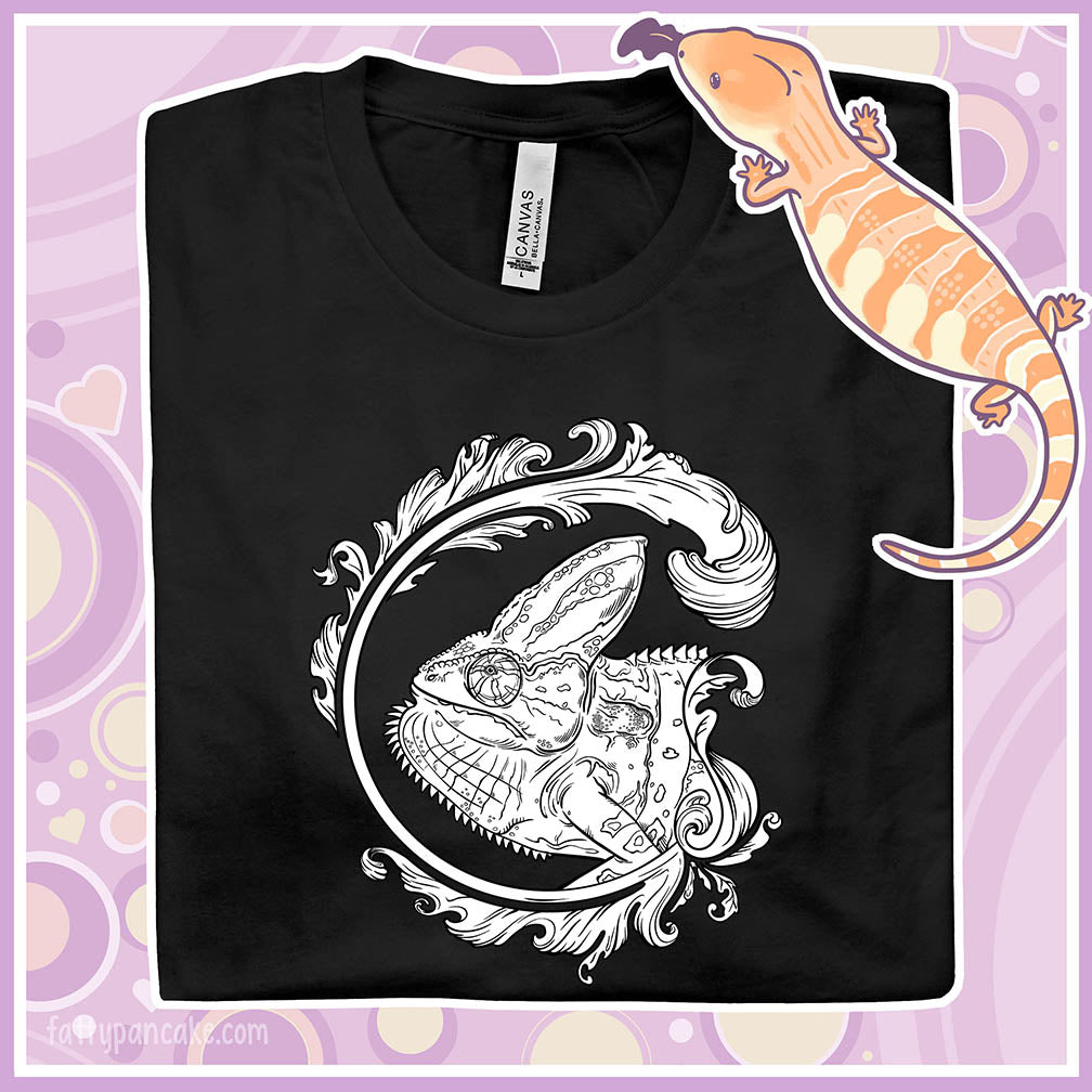 Folded black crew neck tee of a black and white veiled chameleon surrounded by a beautiful flourish design.