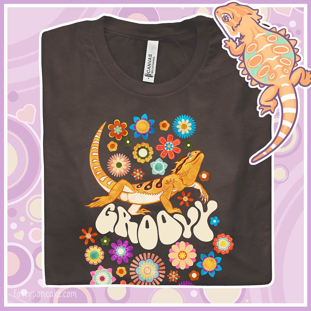 A folded brown crew neck tee showing a groovy bearded dragon design with a 70's retro style with many multi colored flowers surrounding a strutting bearded dragon lizard with the text "groovy" under it's body.