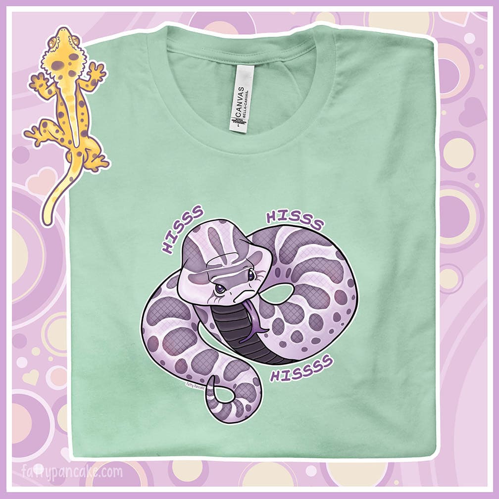 A folded mint colored crew neck tee of a cartoon hognose snake saying hiss hiss hiss!