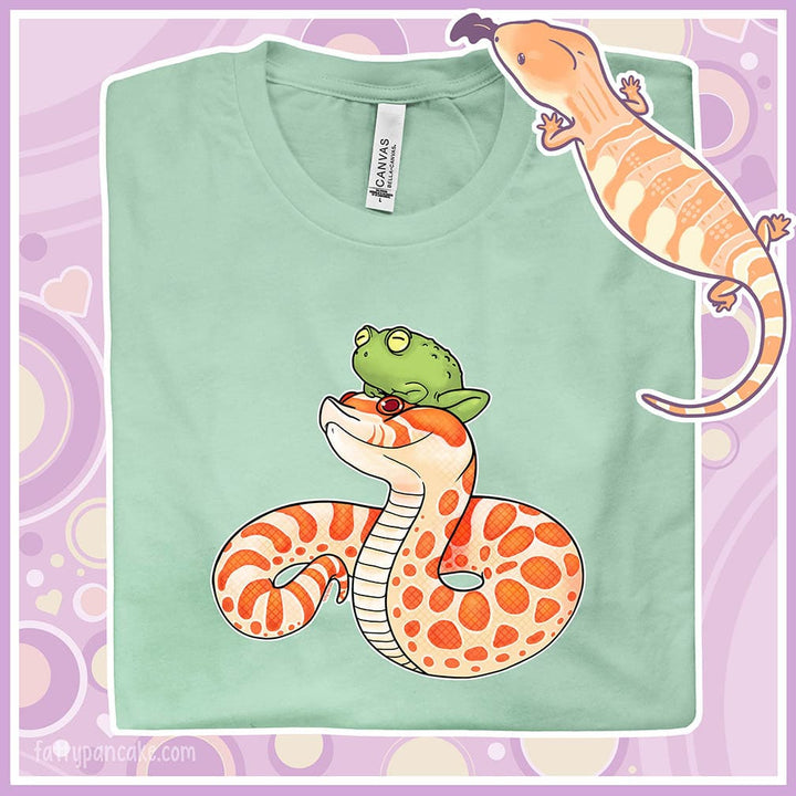 A folded heather prism mint crew neck tee with a cartoon albino hognose snake with a frog perched on it's head.