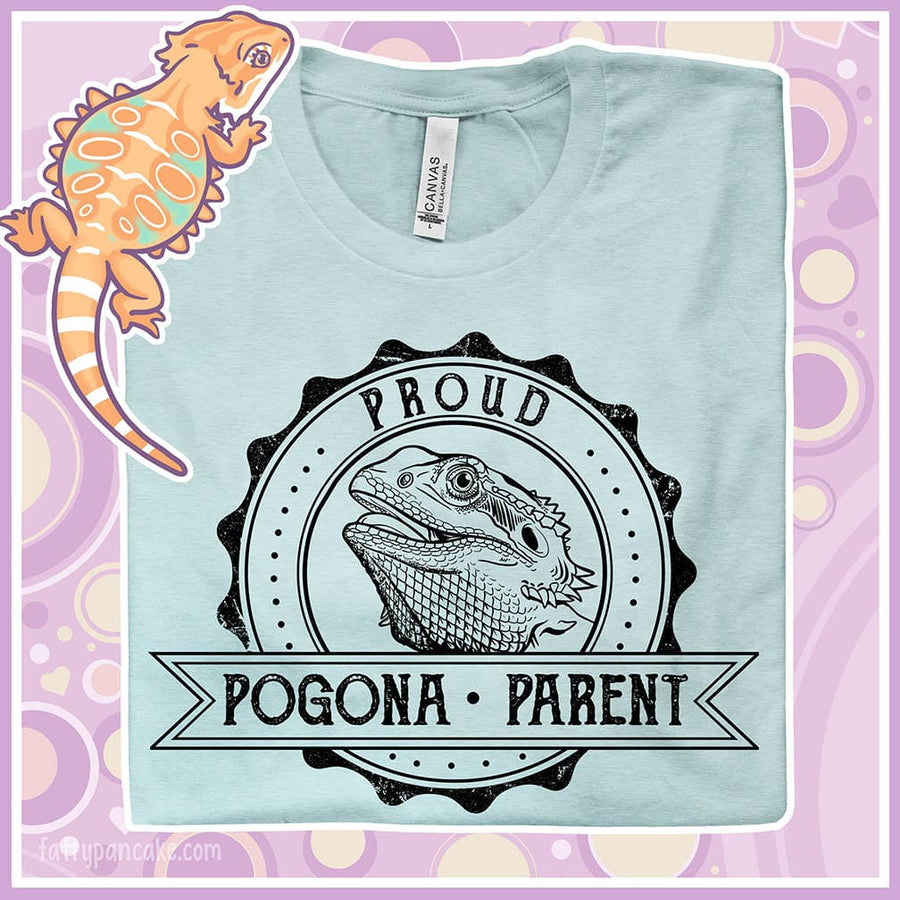 Image of a close up of a heather prism ice blue colored crew neck shirt with a graphic design of a bearded dragon done in black and white centered in a round badge with the text, "Proud Pogona Parent" on the banner design.