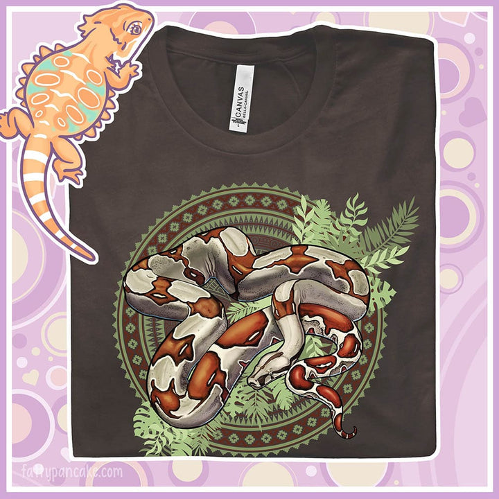 Folded brown colored crew neck tee showing a red tailed boa constrictor in the center of a westernish patterned design with simple leaf graphics under the boa.