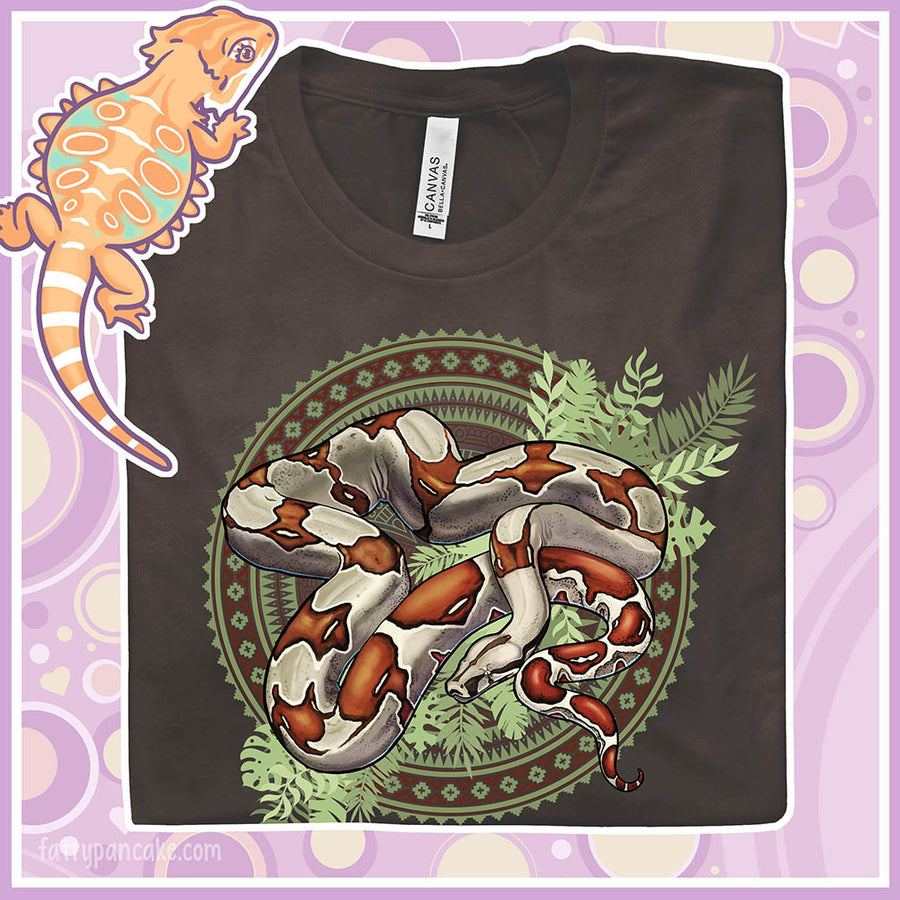 Folded brown colored crew neck tee showing a red tailed boa constrictor in the center of a westernish patterned design with simple leaf graphics under the boa.