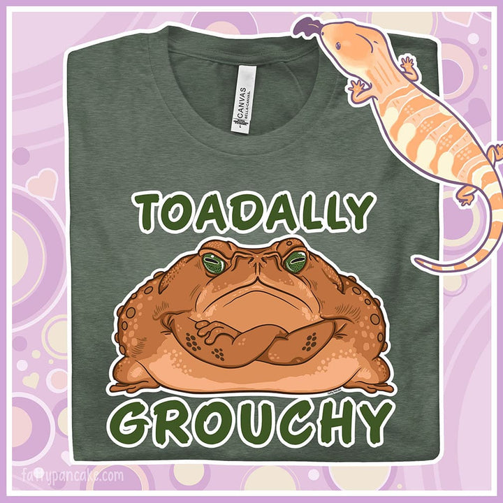 A folded heather green crew neck tee with a grumpy looking cane toad with it's arms crossed and the text Toadally Grouchy above and below it.