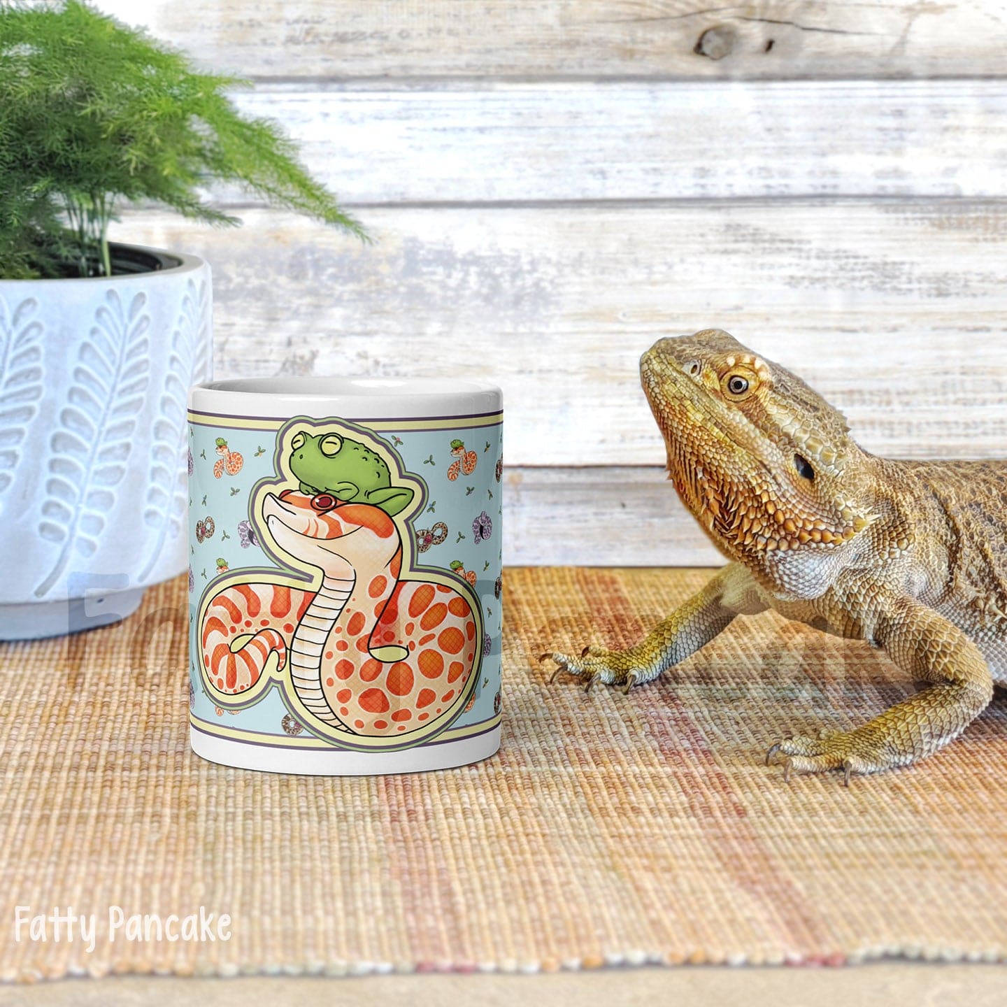 Image of a 11oz mug with a graphic showing an albino hognose snake with a frog on it's head. The background color is blue with lots of other hognose snakes and flowers surrounding it. 