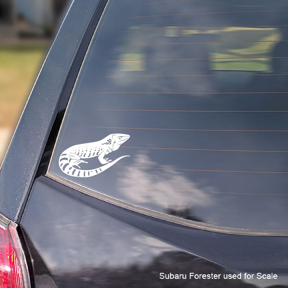 A white vinyl decal of a Dusky Giant Ameiva lizard applied to the rear window of a dark-colored car, shown for scale with a Subaru Forester watermark in the bottom right corner.
