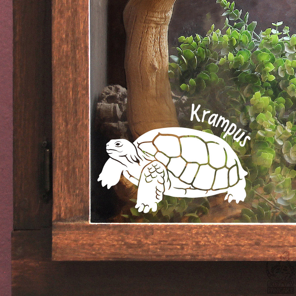 A close up of a wooden reptile enclosure with a white vinyl decal of a Gopher Tortoise with the name Krampus above it&