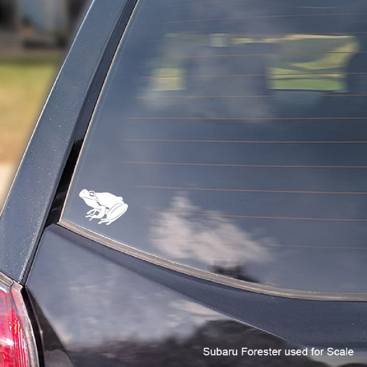 A white vinyl decal of a frog with a car window, shown applied to the rear window of a dark-colored vehicle.