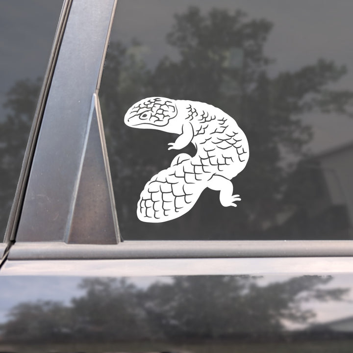 A white vinyl decal of a Shingleback skink lizard applied to the side window of a dark car, with reflections of trees visible in the glass.