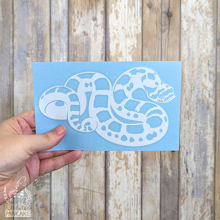 A hand holding a white vinyl hognose snake decal against a white washed wooden background.