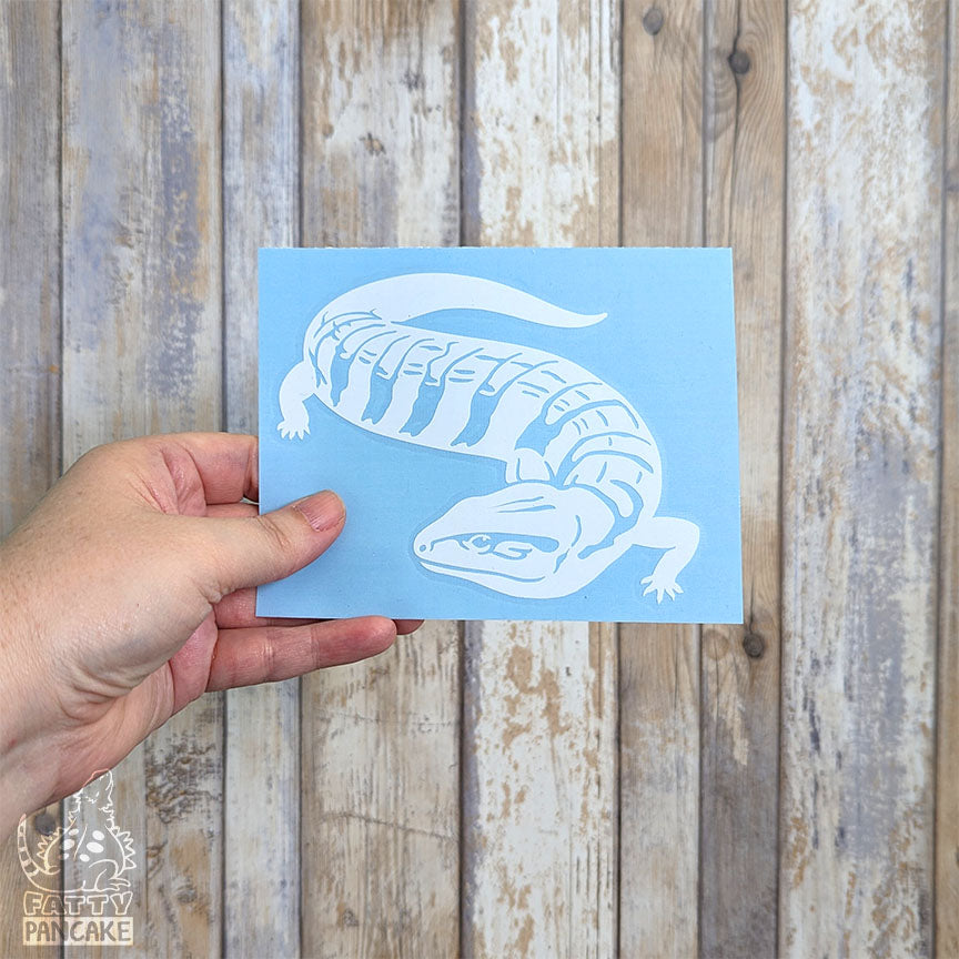 Hand holding a vinyl decal against a white washed wood background.