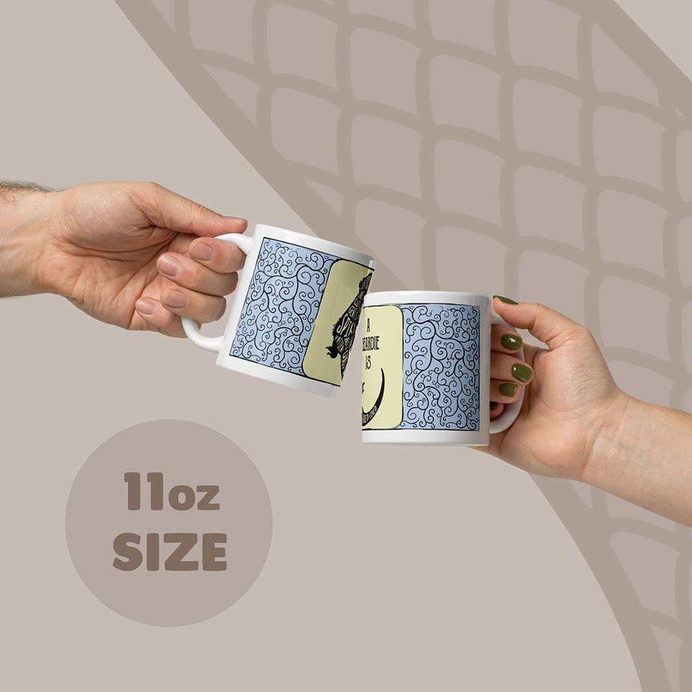Two white ceramic mugs with an 11oz capacity, each featuring a blue and black swirling filigree pattern on the sides. The mugs display a graphic of a bearded dragon with text in the body.