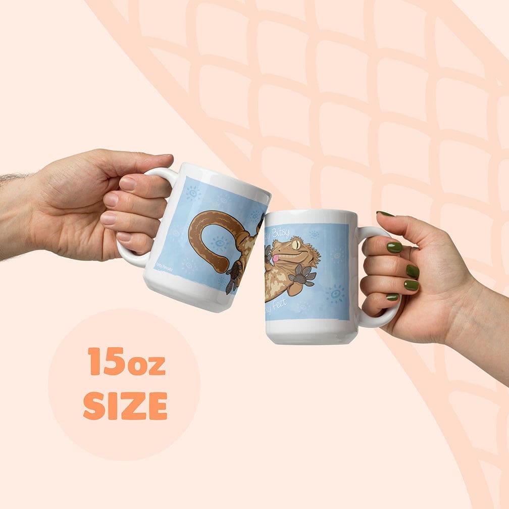 Two hands holding white 15oz mugs with blue cartoon crested gecko illustrations, clinking them together against a pale peach background with a subtle snake scale pattern.
