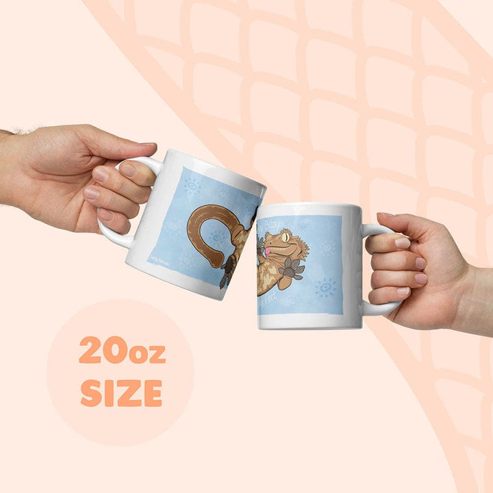 Two hands holding white 20oz mugs with blue cartoon crested gecko illustrations, clinking them together against a pale peach background with a subtle snake scale pattern.