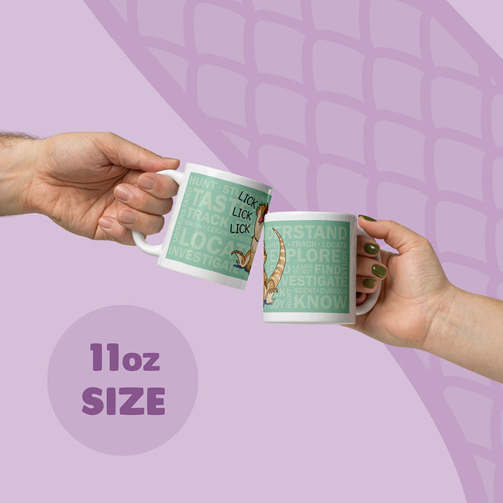 Two white 11oz ceramic mugs being held up by two hands featuring a light green rectangular graphic with the text "HUNT, TASTE, TRACK, LOCATE, INVESTIGATE, UNDERSTAND, EXPLORE, FIND, KNOW" and an illustration of a bearded dragon lizard with the word "LICK".