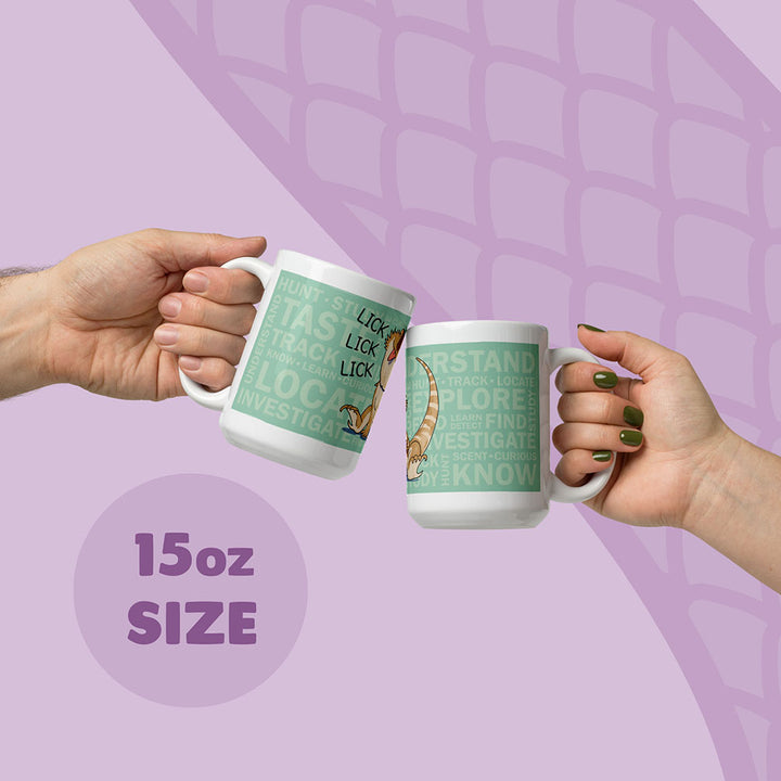 Two white 15oz ceramic mugs being held up by two hands featuring a light green rectangular graphic with the text "HUNT, TASTE, TRACK, LOCATE, INVESTIGATE, UNDERSTAND, EXPLORE, FIND, KNOW" and an illustration of a bearded dragon lizard with the word "LICK".