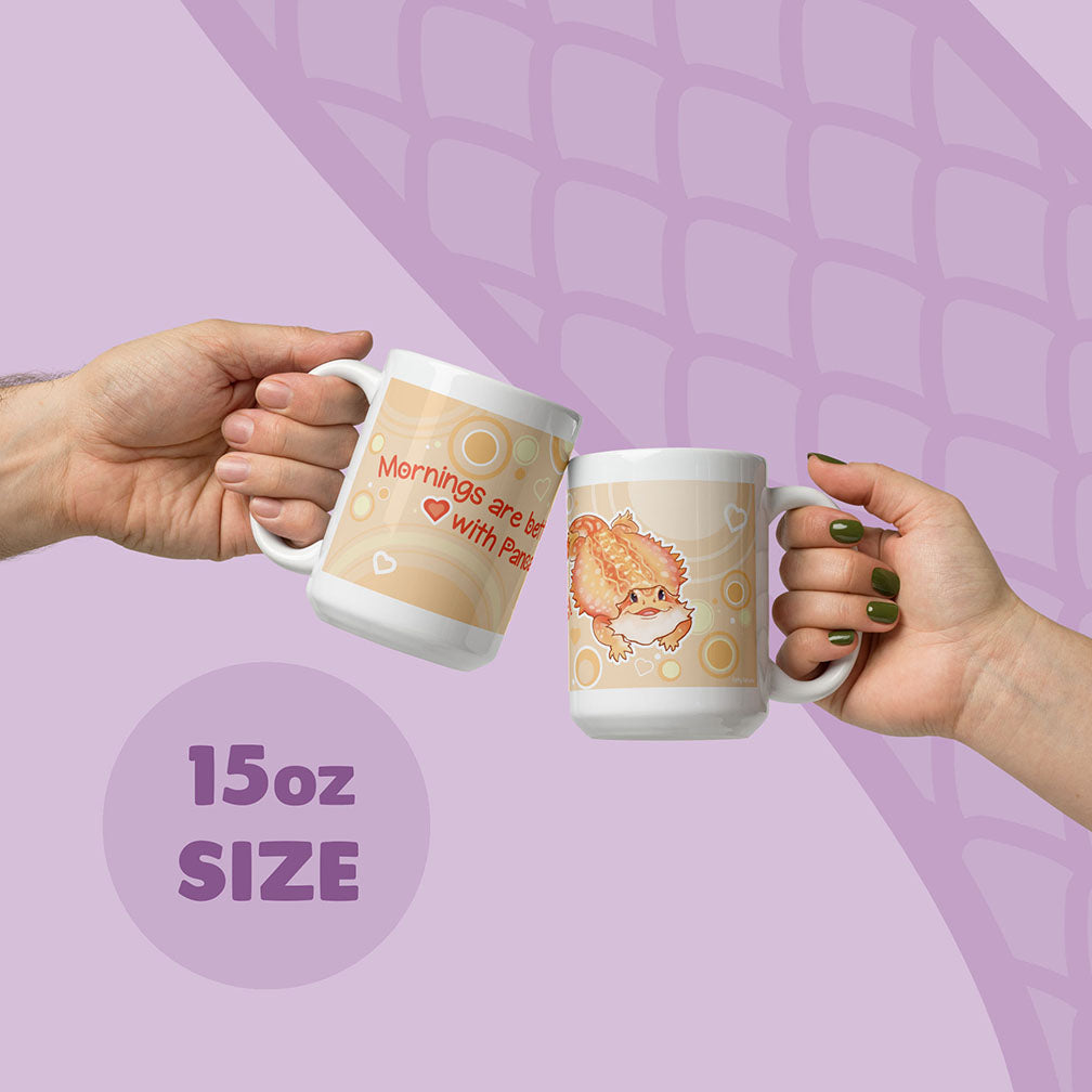 Two hands holding up two 15oz ceramic mugs with cute cartoon bearded dragon and text, set against a light purple background with a subtle scale pattern.