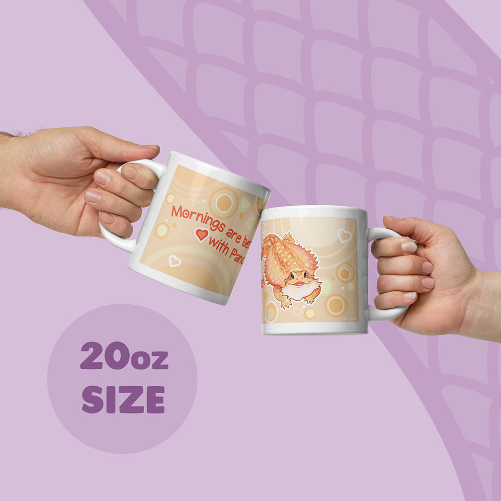 Two hands holding up two 20oz ceramic mugs with cute cartoon bearded dragon and text, set against a light purple background with a subtle scale pattern.