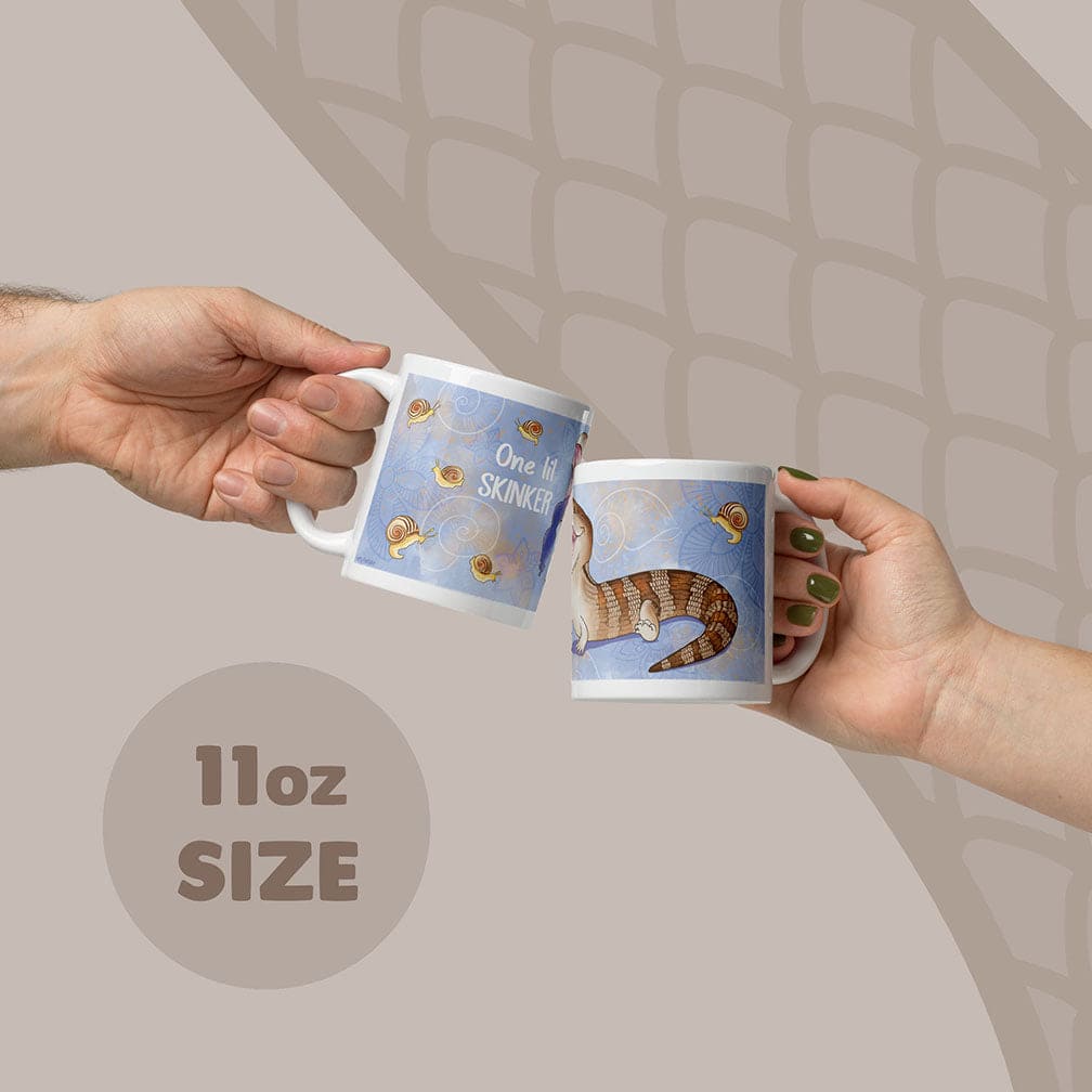 Two white ceramic mugs with an 11oz capacity, featuring a blue background with a brown and tan skink lizard illustration, small snail graphics, and the text One lil SKINKER printed in white on the side of the mugs.