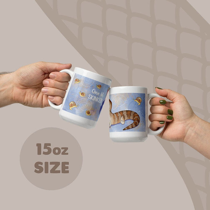 Two white ceramic mugs with an 15oz capacity, featuring a blue background with a brown and tan skink lizard illustration, small snail graphics, and the text One lil SKINKER printed in white on the side of the mugs.