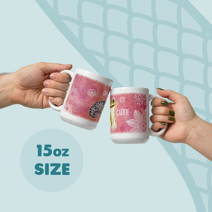 Two white ceramic mugs with a pink floral background and a leopard gecko illustration. The mugs feature the text OH CUTE and are labeled as 15oz size. The design includes white line-art flowers and a spotted gecko pattern on the surface.
