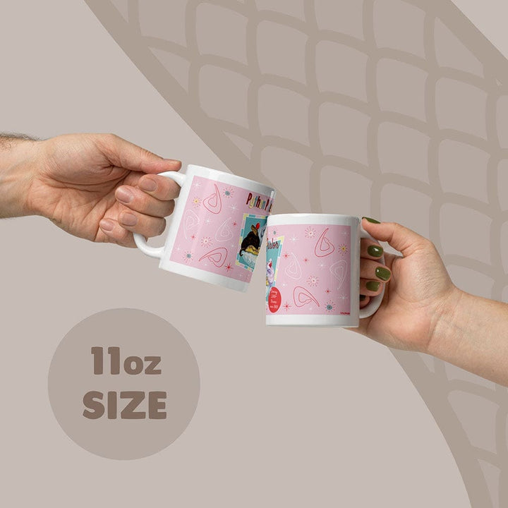 Two white ceramic mugs with a pink design being held by two hands, with an 11oz capacity label on the bottom of the image.
