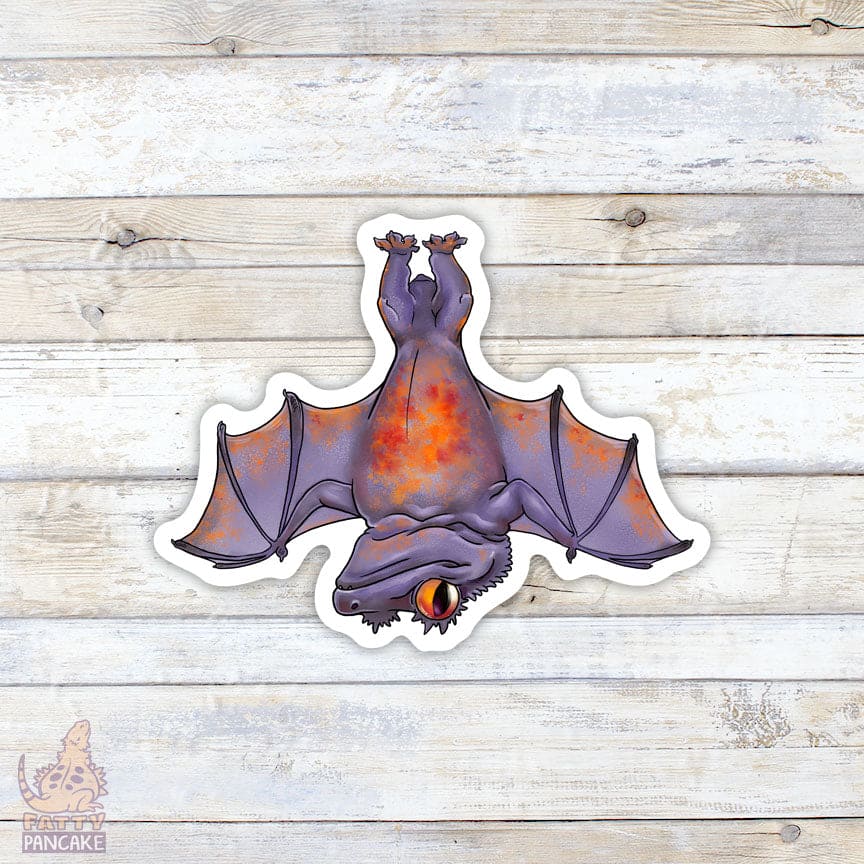 A Halloween themed sticker of a crested gecko with bat wings, hanging upside down. It has a purple color with bright red and oranges on it's belly and it's wings are outstretched.