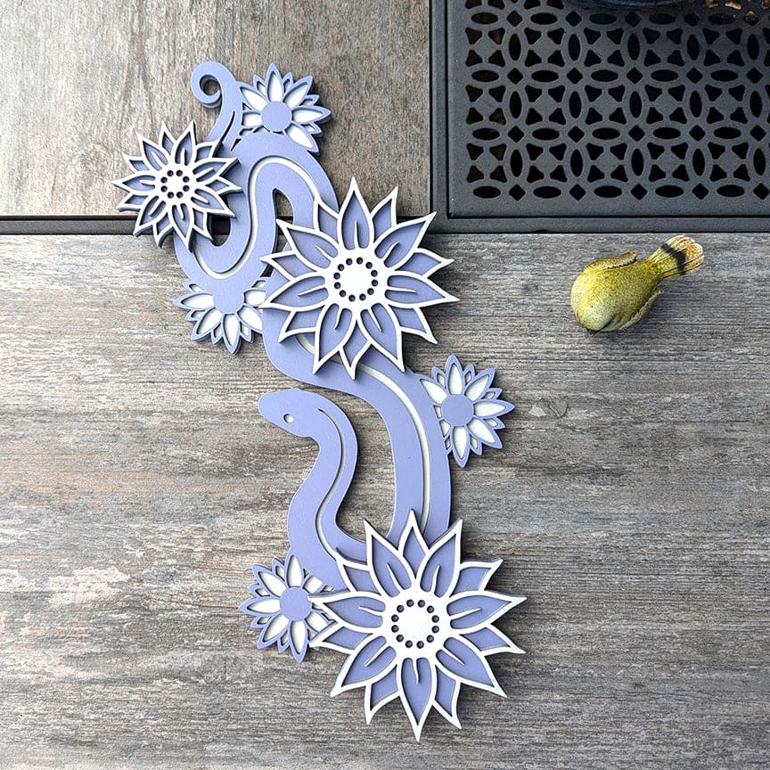 Decorative wood snake with flowers wall hanging art piece in lavender color placed on a slate tile on a table.