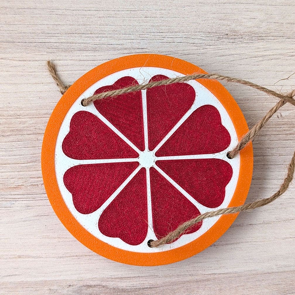 Decorative grapefuit slice ornament with string on a wooden surface.