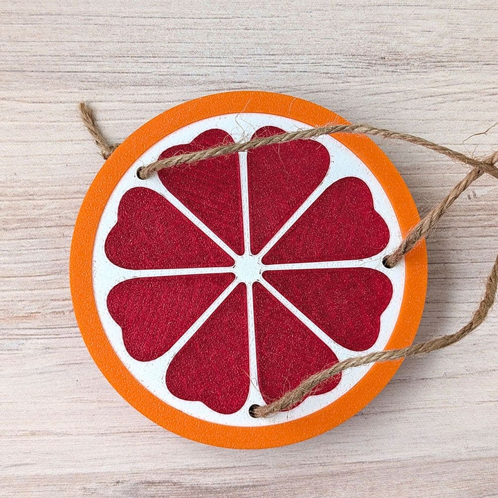 Decorative grapefuit slice ornament with string on a wooden surface.