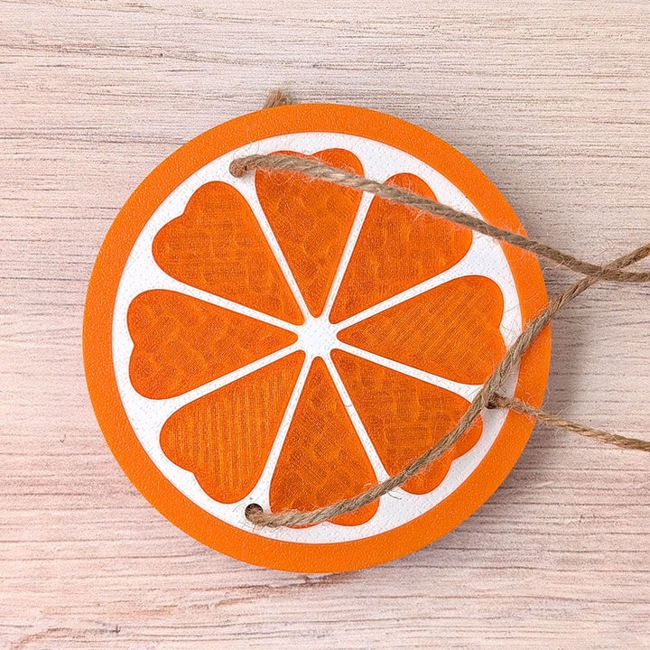 Decorative orange slice ornament with string on a wooden surface.