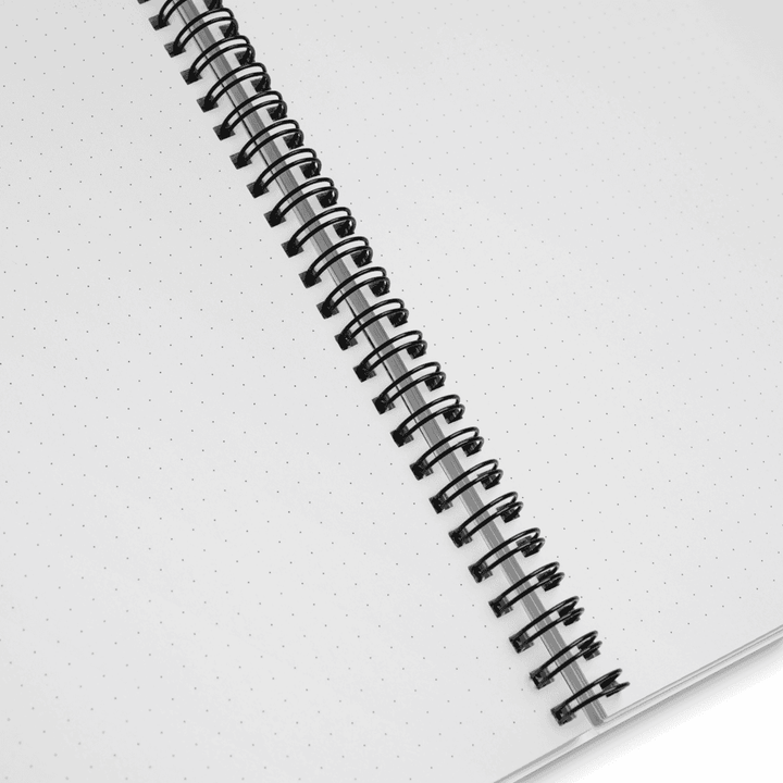 Spiral-bound notebook with a white background. The close up shows the paper has dots for writing or drawing.