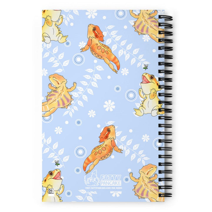 A spiral-bound notebook with a light blue cover decorated with cartoon bearded dragons and white floral motifs, shown on a plain white background. The Fatty Pancake logo is on the bottom center of the design.