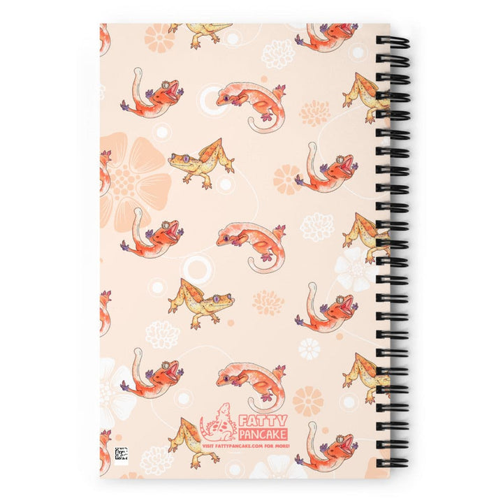 A spiral-bound notebook with a peach-colored cover featuring a repeating pattern of orange geckos and white floral motifs. The cover has a black spiral binding on the right side and a &