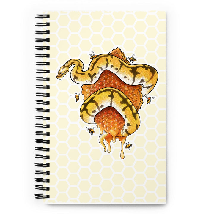 A spiral-bound notebook with a pale yellow honeycomb pattern cover, featuring an illustration of a yellow and black snake wrapped around a honeycomb structure. The notebook is displayed on a bright white background.