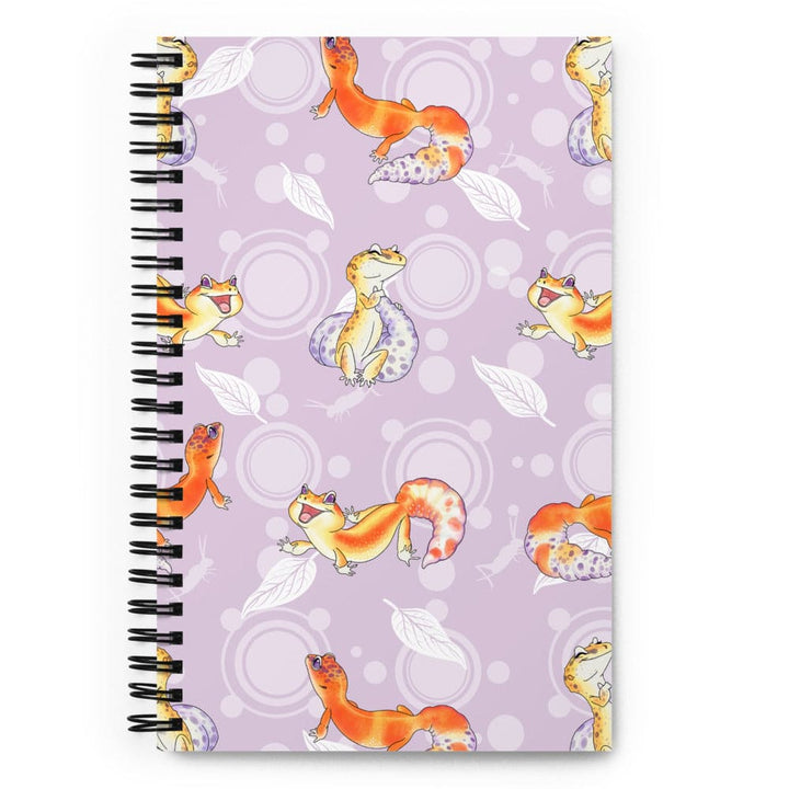 A spiral-bound notebook with a lavender cover decorated with a repeating pattern of orange and yellow leopard geckos, white leaves, and light purple circles, shown on a plain white background.