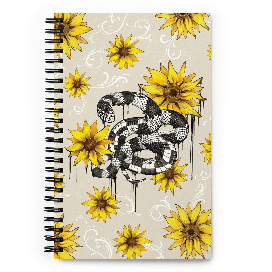 A spiral-bound notebook with a beige cover featuring a black and white snake illustration and yellow sunflower designs, displayed on a bright white background.